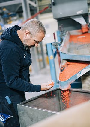 Polykemi employee checking orange plastic compound pellets coming out of a machine