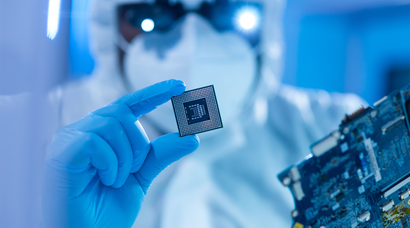 Image of a laboratory professional holding a microchip in their hand and inspecting with magnifying glasses to support chip manufacturing article
