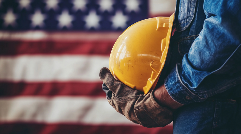 Manufacturing worker holding hard hat in front of American flag to support October PMI article