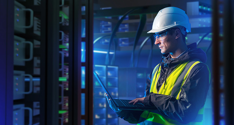 Man with laptop in server room. System administrator for industrial companies. Guy with computer. Server racks emit neon light. Maintenance industrial server equipment. Man in helmet in data center