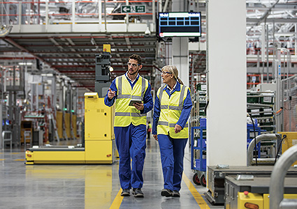 Male and female factory workers walking through a factory discussing seriously while using a digital tablet