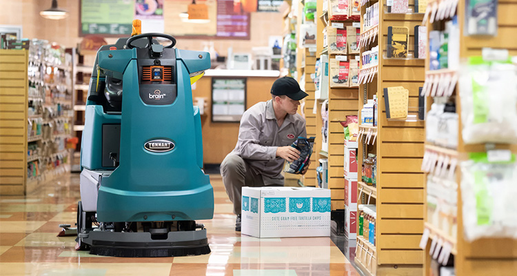 A WORKER CROUCHES IN A SUPERMARKET AISLE NEXT TO AN AUTONOMOUS MOBILE ROBOT