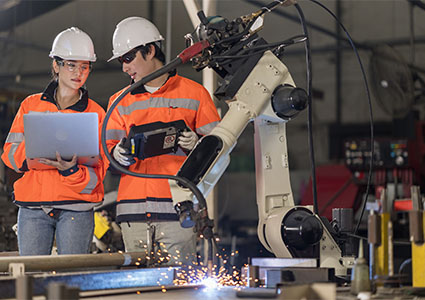 Two Industrial Engineers holding the Laptop Computer examining the operating Robotic welding Machine in the factory. Welding robotics for small manufacturing. Product Quality and Precision Control Process