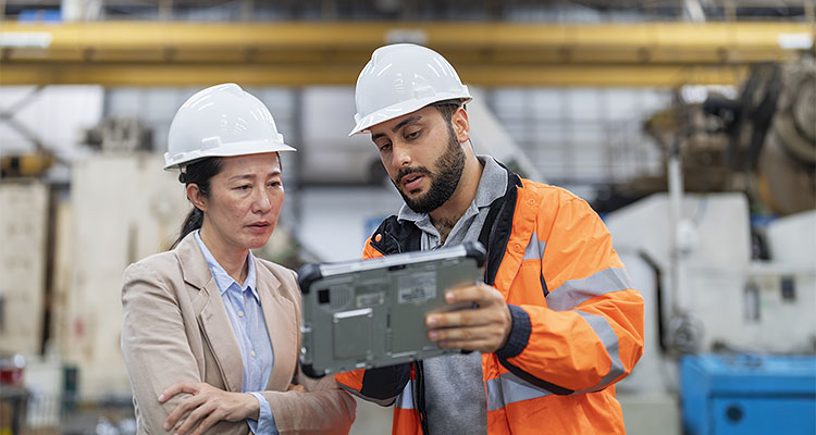 Two workers in white hard hats looking at tablet one in a high visibility jacket