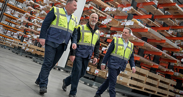 Three men in high visibilty jackets walking through a warehouse