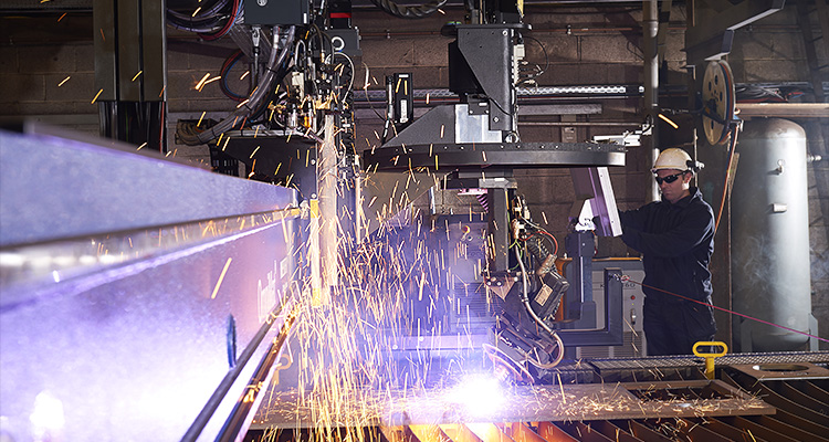 industrial welding or cutting operation, likely involving a plasma or oxyfuel cutting machine, with a worker observing the process