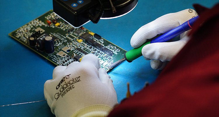 technician soldering on a printed circuit board (PCB) under a microscope