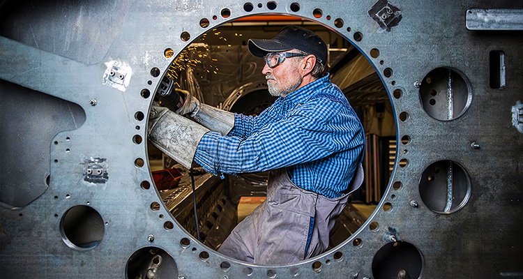 worker using a tool inside a large piece of industrial machinery