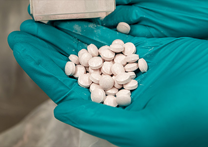  a quantity of paracetamol pills being held in a gloved hand. 