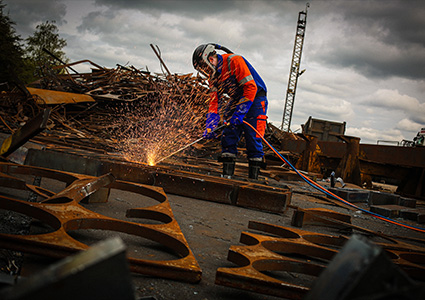 a worker performing metal cutting at a scrap metal recycling facility