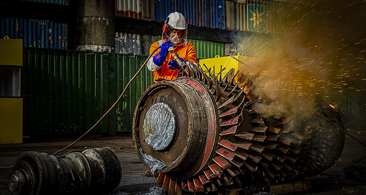 a worker performing maintenance on a large turbine rotor assembly.