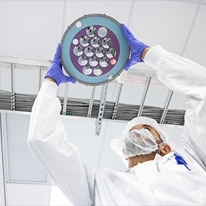 a technician in a cleanroom inspecting a dome rack loaded with optical lenses