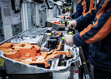 workers assembling high-voltage battery packs for electric vehicles on a production line. 