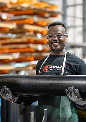 an employee from Morton Industries smiling while holding a large black industrial pipe