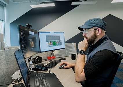 a man sitting at a desk in an office environment, focused on multiple computer screens