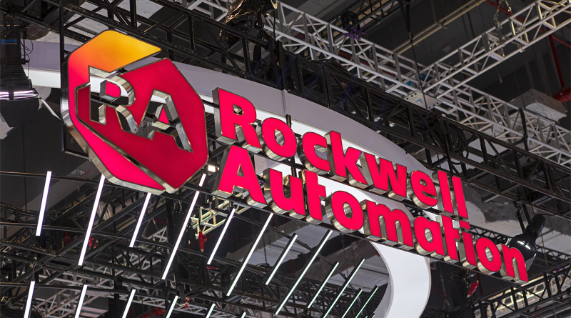 Rockwell Automation logo displayed on a large illuminated sign at an industrial trade show booth with metal truss structures and lighting overhead.