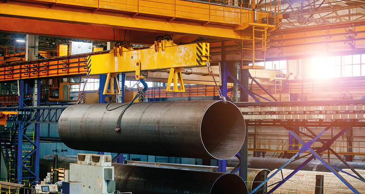 a large overhead gantry crane transporting a heavy metal steel pipe