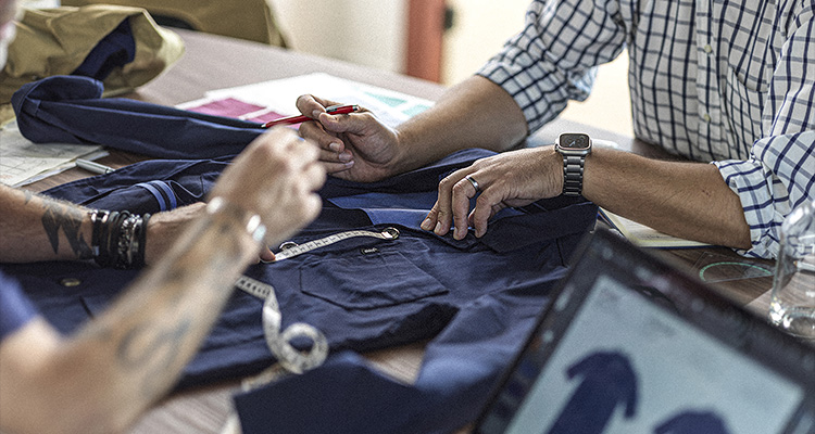 two people working closely on a dark navy blue garment spread across a wooden table