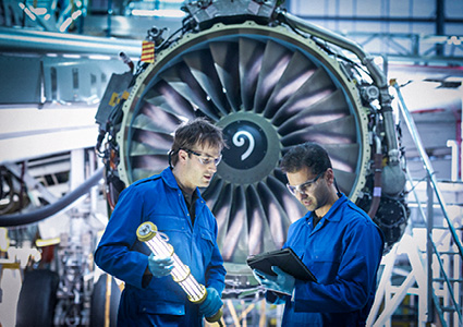 two aircraft maintenance technicians or engineers in blue coveralls working in an industrial hangar