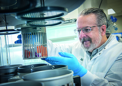 a cientist's focus is on a piece of laboratory equipment, specifically a cylindrical rack or holder that contains several test tubes or vial