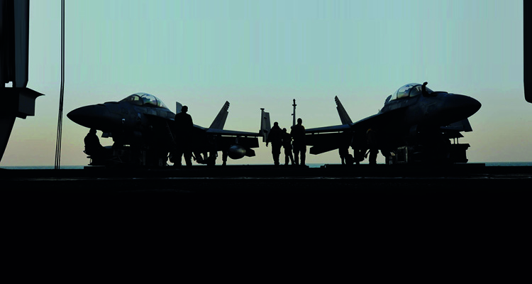 a silhouette of two Grumman F-14 Tomcat fighter jets parked on the flight deck of an aircraft carrier