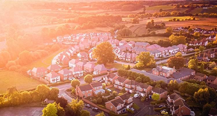 an aerial, high-angle photograph of a suburban neighborhood bathed in the warm, golden light of a sunrise or sunset