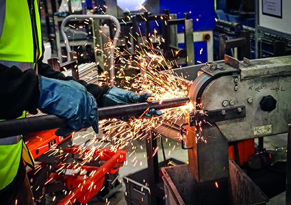 A worker is operating a heavy-duty industrial belt grinder to shape or finish a metal component