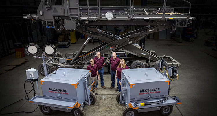 four people standing in front of heavy industrial machinery inside a large warehouse or hangar.