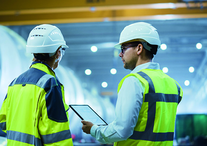 Two individuals in industrial safety gear reviewing data on a tablet device