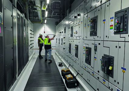 industrial technicians performing maintenance on a large, wall-mounted electrical switchgear panel