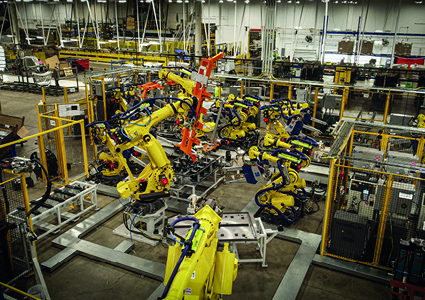 a complex automated assembly cell populated by multiple industrial robotic arms inside a manufacturing plant