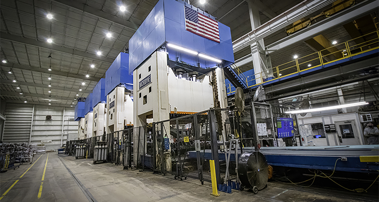 a row of massive industrial hydraulic stamping presses operating inside a large manufacturing plant