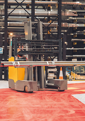 an industrial warehouse setting where a worker is operating a specialized forklift to move heavy metal stock