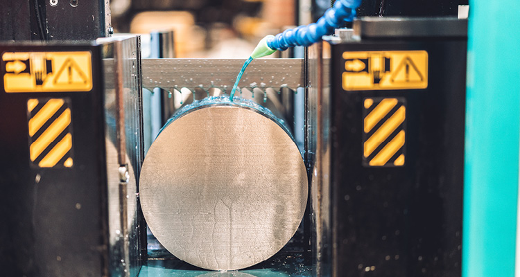 Aligning unparalleled passion with technical excellence, Dynamic Metals does whatever it takes to support its customers an industrial horizontal band saw cutting through a thick, solid cylindrical metal bar.