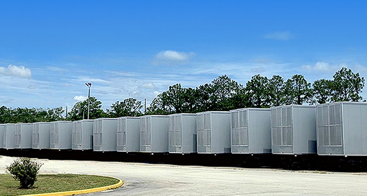 a long, uniform row of large industrial utility enclosures or modular units installed outdoors on a paved lot
