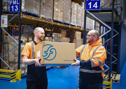 two warehouse workers happily collaborating inside a large logistics facility.