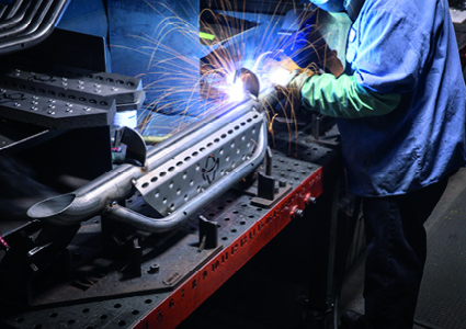  a worker welding a metal automotive or mechanical component on a heavy-duty workbench