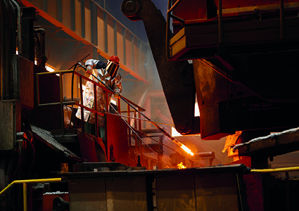 a steelworker in protective gear operating an industrial furnace