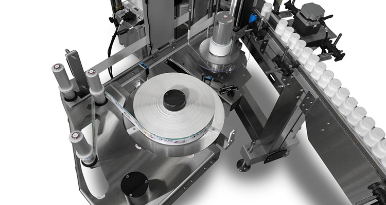 a top-down perspective of an automated industrial labeling machine processing small bottles on a production line