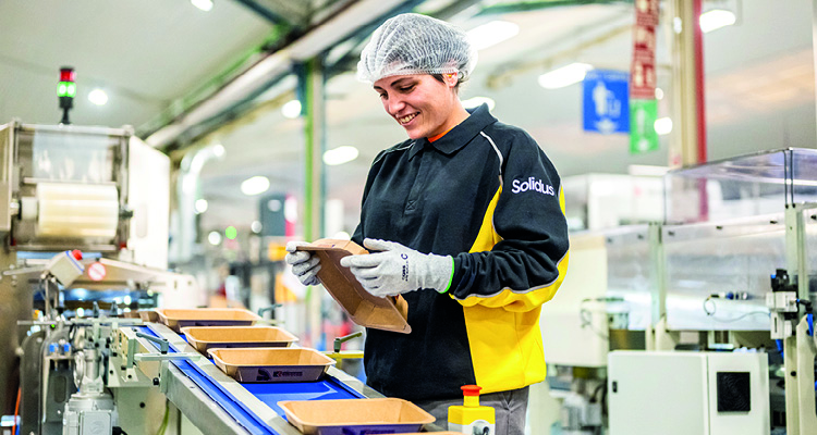 a factory worker conducting a quality check on sustainable food packaging along an automated assembly line