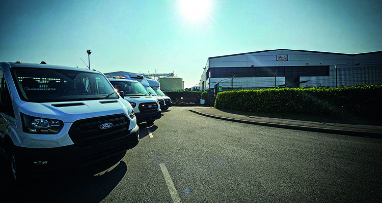 As it enters the electric vehicle market, VFS is rethinking its entire processes and operations a commercial facility on a bright, sunny day, showcasing a fleet of Ford Transit commercial vans