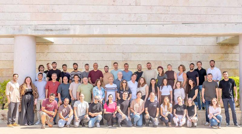 Large team group photo of employees gathered outdoors in front of a modern stone building.