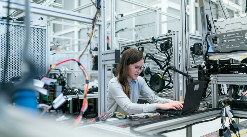 Manufacturing engineer using a laptop beside industrial equipment during a quality control process.