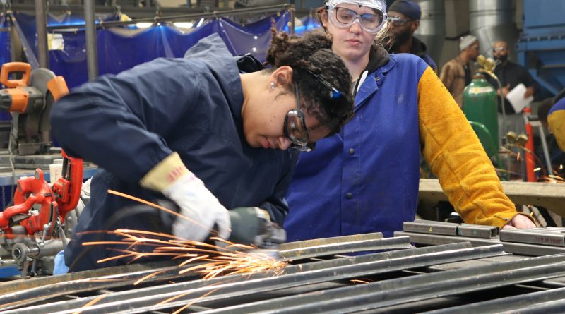 Manufacturing workers wearing safety equipment during hands-on metalworking training on a factory floor.