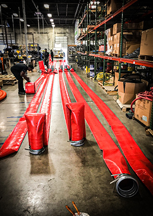 long, bright red industrial layflat hoses or floating PVC containment barriers laid out on a warehouse floor