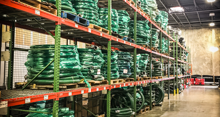 an industrial warehouse interior with heavy-duty metal shelving racks stacked with coiled green hoses and industrial tubing