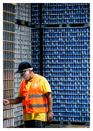 a worker in an industrial warehouse standing next to large, stacked pallets of blue beverage cans