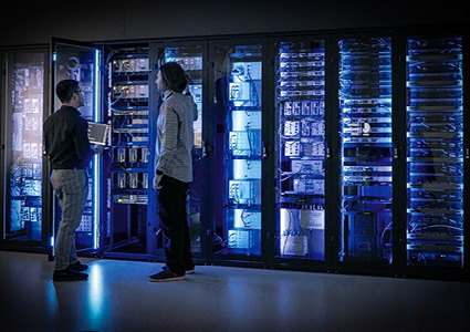 technicians working in a server room or data center facility with rows of enclosed server racks lit by blue ambient lighting