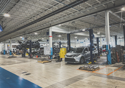 a large, modern indoor automotive service center with white tiled floors, exposed ceiling joists, and multiple car lifts
