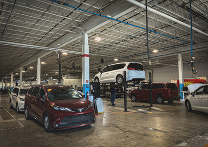 a service center with vehicles parked and on a lift inside a large garage with an industrial ceiling